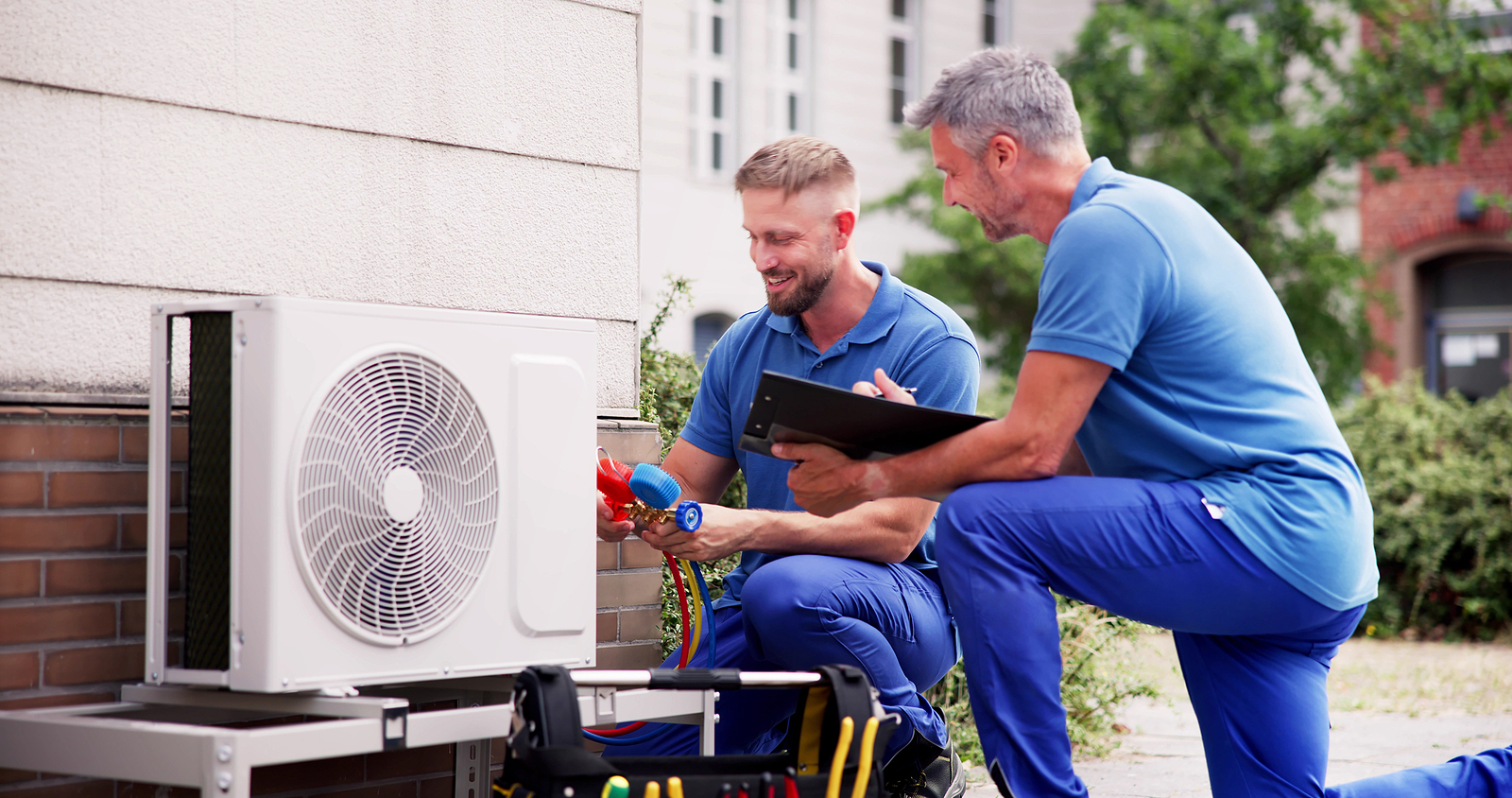 Two workers on the roof of a building working on the air conditioning unit.